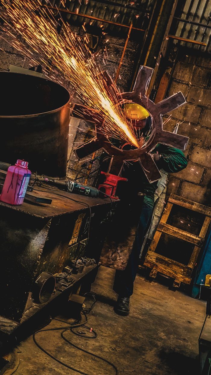 A welder uses a grinder in a dimly lit factory, creating a spectacular shower of sparks.