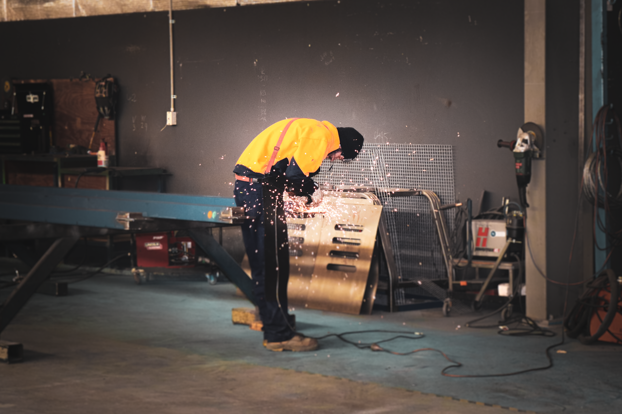 A metalworker grinding metal in an industrial workshop, creating bright sparks.
